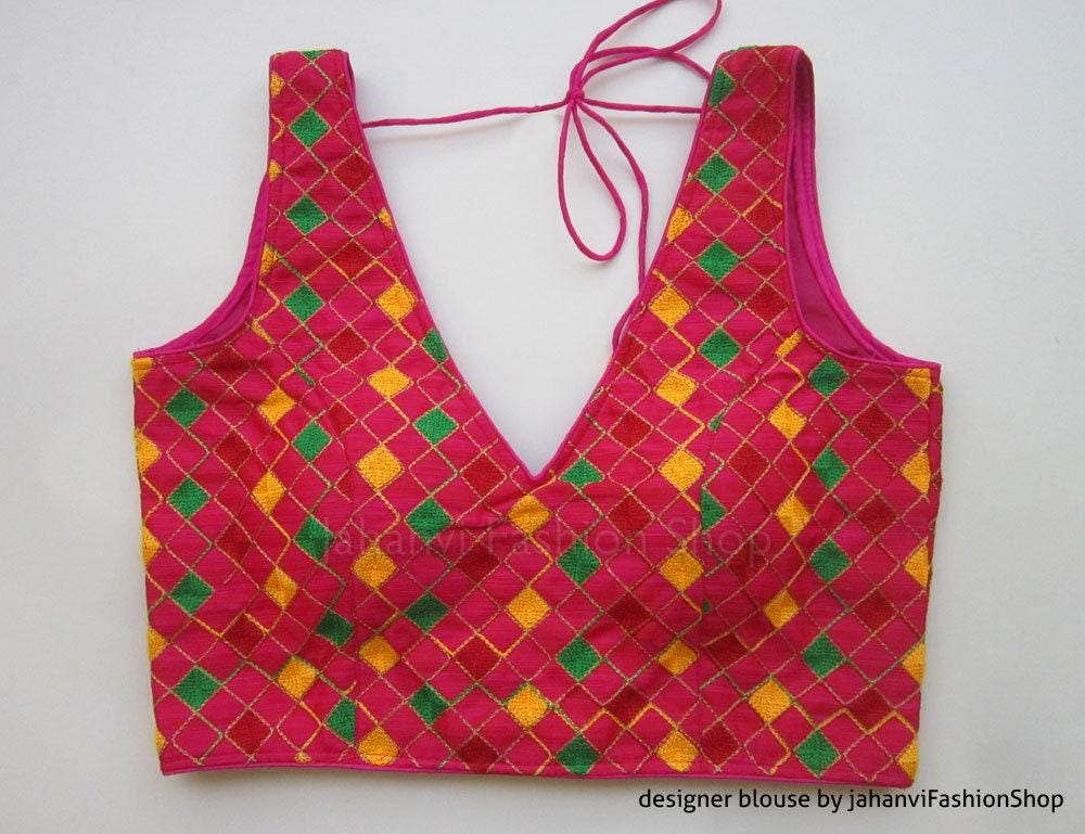 Magenta sleeveless saree blouse with V neckline, bow tie straps, geometric green and yellow embroidery