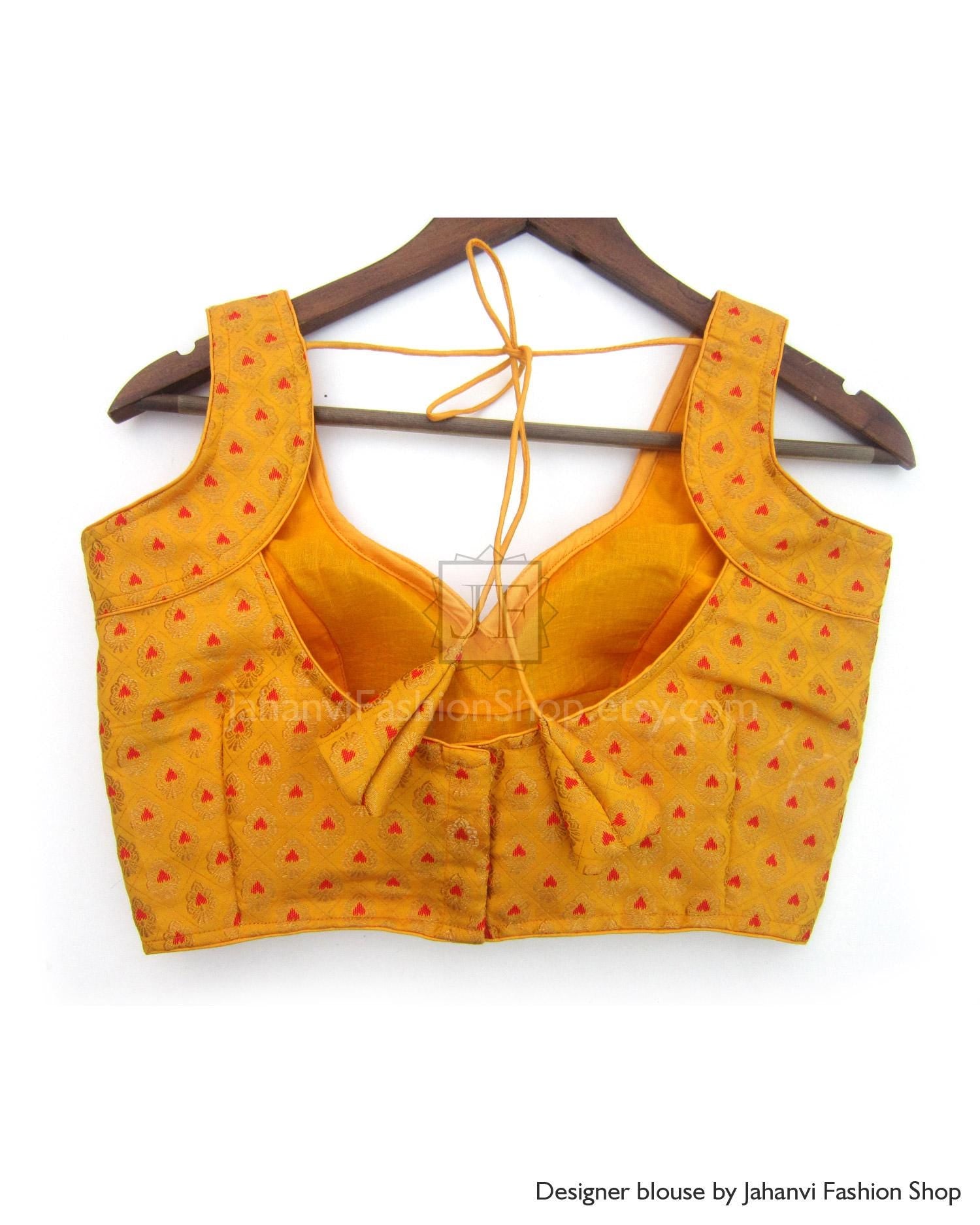 Orange embroidered sleeveless blouse with open back and tie neck, on a hanger